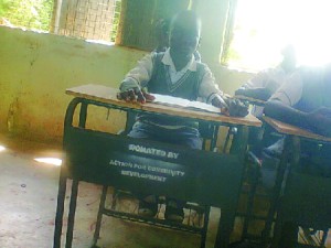 student of Oghede Community Secondary School, on one of the chair and desk donated.